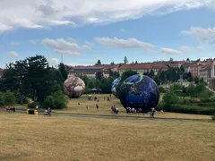 Velké zeměkoule jako umělecká instalace v parku s lidmi a budovami v pozadí