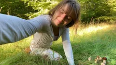 Žena sbírá houby v lese, slunečný den, tráva, lesní prostředí, houbaření v přírodě.