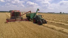Biofarmář sklízí obilí na hnědém poli s červenými a zelenými kultivátory